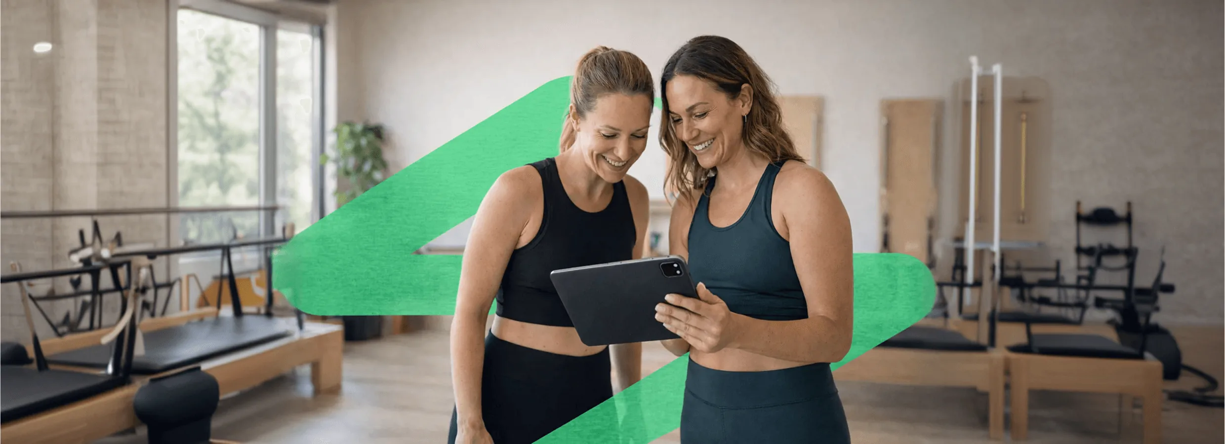 Pilates stüdyosunda tabletten Fitjourney panelini inceleyen iki kadın
